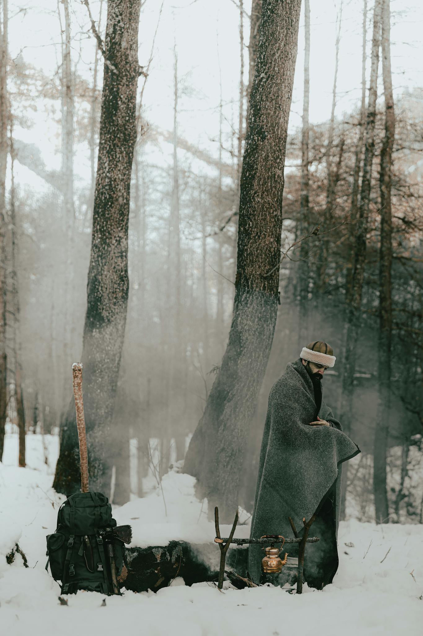 A person wrapped in a blanket standing by a campfire in a snowy forest.