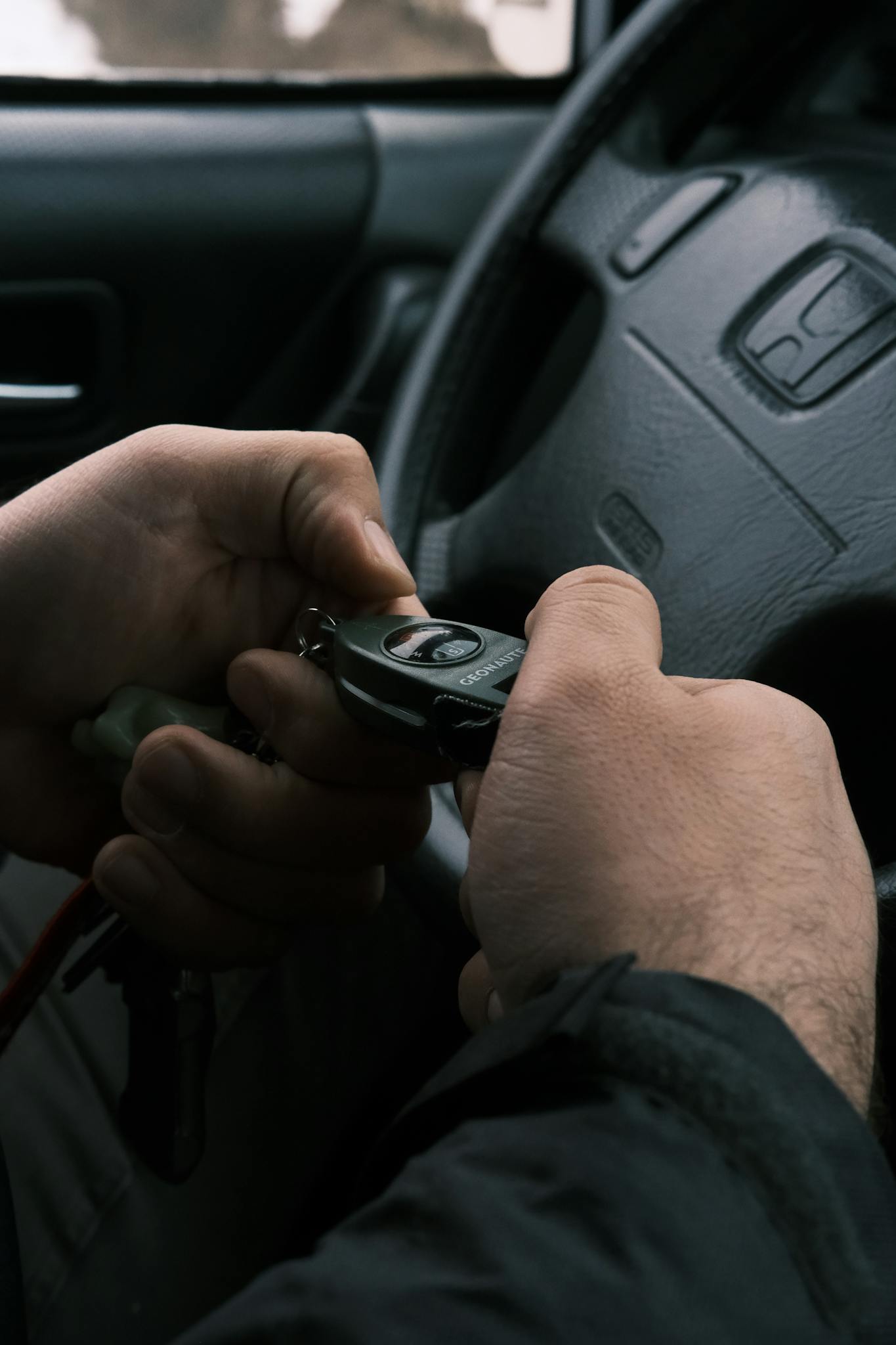 Close-up of hands holding a compass in a car interior setting, hinting navigation.